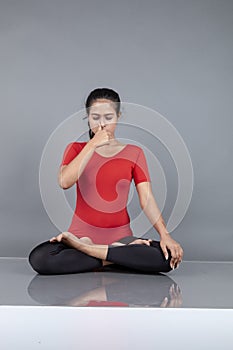 Healthy young woman in red t-shirt and black leggings doing yoga and stretching exercises isolated on grey background