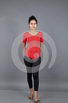 Healthy young woman in red t-shirt and black leggings doing yoga and stretching exercises isolated on grey background