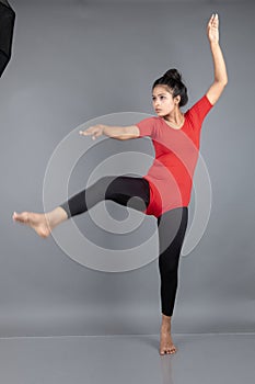 Healthy young woman in red t-shirt and black leggings doing yoga and stretching exercises isolated on grey background