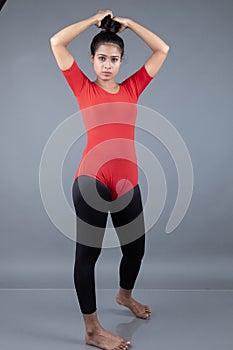 Healthy young woman in red t-shirt and black leggings doing yoga and stretching exercises isolated on grey background