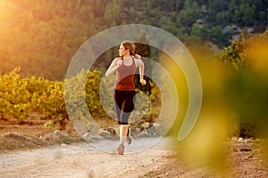 Healthy young woman running on dirt road in countryside