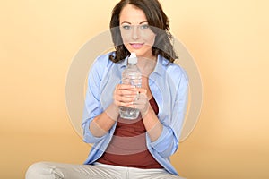 Healthy Young Woman Sitting on Floor Holding a Bottle of Still Mineral Water