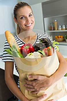 Healthy young woman with vegetables in grocery bag in the kitchen at home.