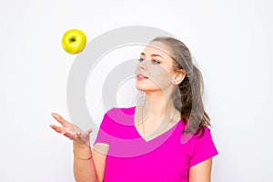 Healthy young woman wearing in pink shirt throwing up green apple