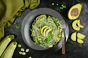 Healthy Zucchini Noodles with Basil Pesto, Beans, Brussels Sprouts and Avocado - served on a black background