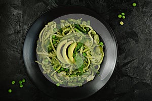 Healthy Zucchini Noodles with Basil Pesto, Beans, Brussels Sprouts and Avocado - served on a black background