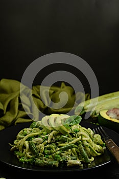 Healthy Zucchini Noodles with Basil Pesto, Beans, Brussels Sprouts and Avocado - served on a black background