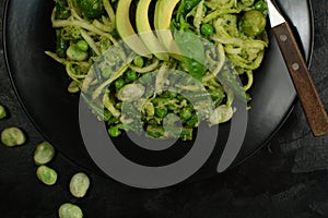 Healthy Zucchini Noodles with Basil Pesto, Beans, Brussels Sprouts and Avocado - served on a black background