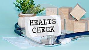 HEALTS CHECK - text on card on wooden table with stethoscope, medical mask and wooden blocks on background