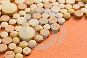 Heap of assorted beige capsules on orange table.