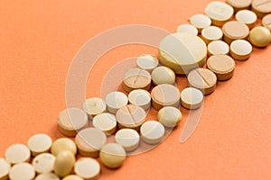 Heap of assorted beige capsules on orange table.