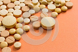 Heap of assorted beige capsules on orange table.