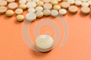 Heap of assorted beige capsules on orange table. One pill is apart, isolated.