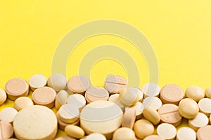 Heap of assorted beige capsules on yellow background.