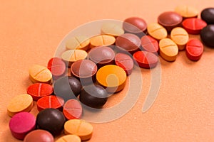 Heap of assorted brown, orange and red capsules on orange table.