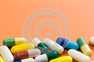 Heap of assorted colorful capsules on orange background.