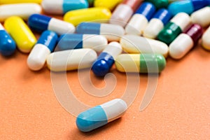 Heap of assorted colorful capsules on orange background. One blu