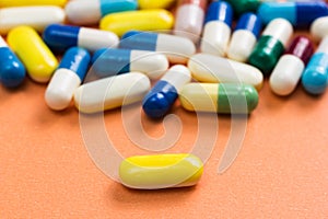 Heap of assorted colorful capsules on orange background. One yel