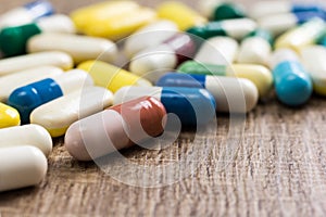 Heap of assorted colorful capsules on wooden background.