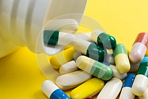 Heap of assorted colorful capsules on yellow table.
