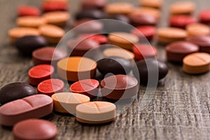 Heap of assorted orange, brown and red capsules on wooden table.