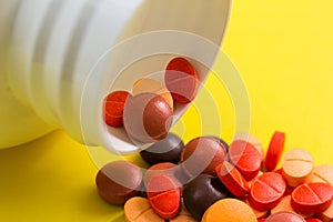 Heap of assorted orange and red capsules on yellow table.