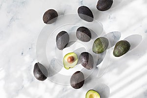 Heap of avocados whole and half on stone table in aesthetic shadow sunlight top view