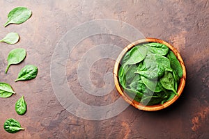 Heap of baby spinach leaves in wooden bowl on rustic stone table top view. Organic healthy food.