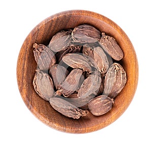 Heap of black cardamom pods in wooden bowl, isolated on white background. Black cardamon seeds. Clipping path. Top view.
