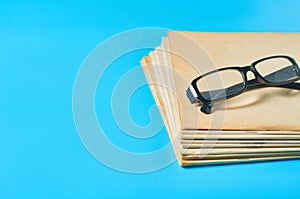 Heap of blank magazines, newspapers or some documents and modern glasses on blue desk