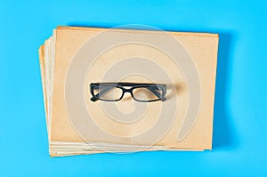 Heap of blank magazines, newspapers or some documents and modern glasses on blue desk