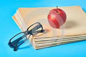 Heap of blank magazines, newspapers or some documents and modern glasses, red apple on blue desk