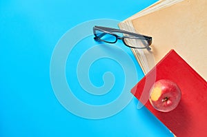 Heap of blank magazines, newspapers or some documents and modern glasses, red apple, book on blue desk