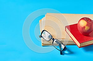 Heap of blank magazines, newspapers or some documents and modern glasses, red apple, book on blue desk