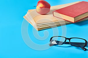 Heap of blank magazines, newspapers or some documents and modern glasses, red apple, book on blue desk