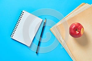 Heap of blank magazines, newspapers or some documents and red apple, notepad, pencil on blue desk