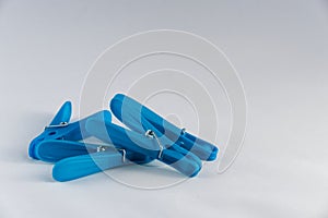 A heap of blue plastic clothes pegs (clothes pins), stacked randomly against a white background