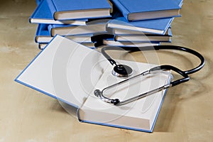 Heap of books reading on a wooden table. Beside lies and stethoscope. Black background.