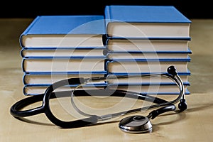 Heap of books reading on a wooden table. Beside lies and stethoscope. Black background.