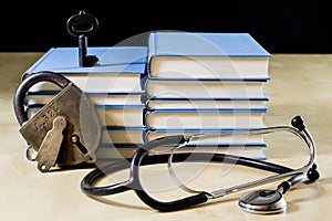 Heap of books reading on a wooden table. Beside lies and stethoscope. Black background.