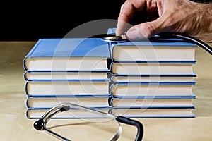 Heap of books reading on a wooden table. Beside lies and stethoscope. Black background.