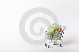 heap of color macaroons in a toy shopping cart on white background