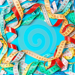 Heap of colorful measuring tapes in the form of frame on turquoise background. Top view of slim waist concept with copy space