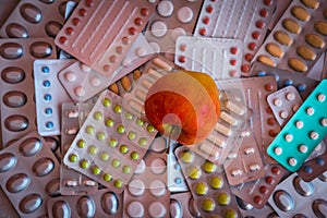 Heap of colorful tablets and capsules in blister and apple in center