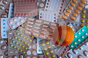 Heap of colorful tablets and capsules in blister and apple in the right bottom corner