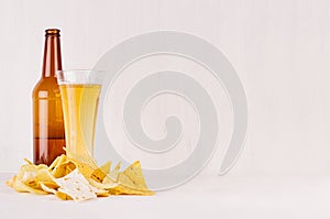 Heap different crispy golden snacks and beer in glass, brown bottle on soft white wood background, with copy space.