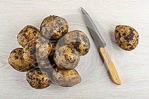 Heap of dirty unpeeled potatoes, knife on wooden table. Top view