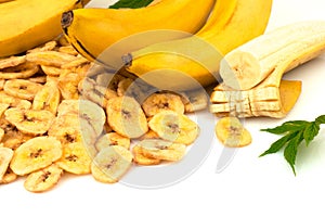 Heap of dried banana chips with yellow banana bunch and green leaves