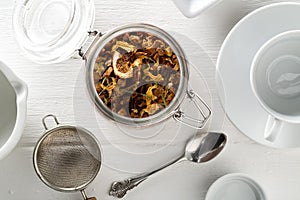 Heap of dried fruit tea infusion with oranges and strawberries mixed with tea leaves and assorted herbs in glass on white wooden