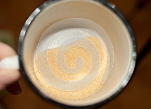 Heap of dry small gelatine granules or powder in a mug, top view photo